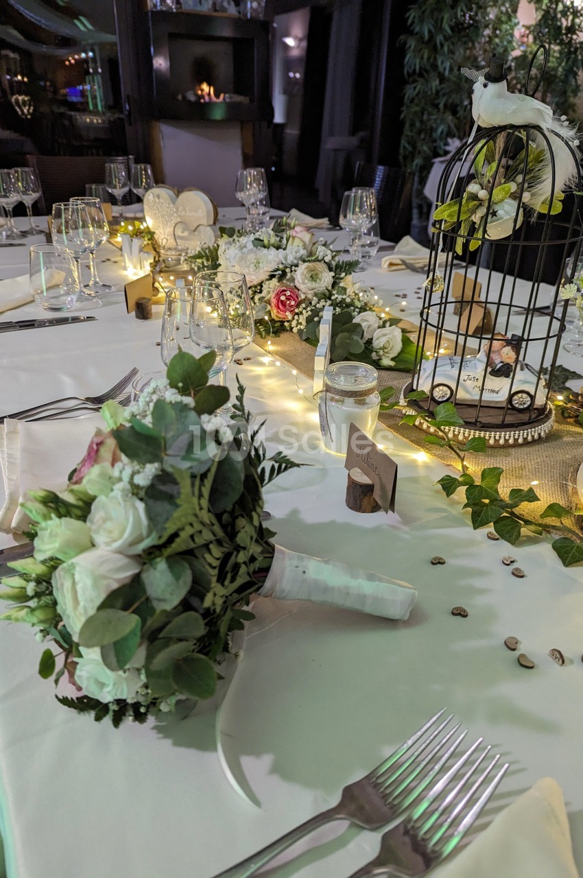 Table décorée pour un mariage avec fleurs, bougies, une cage ornée et un bouquet de mariée au premier plan.