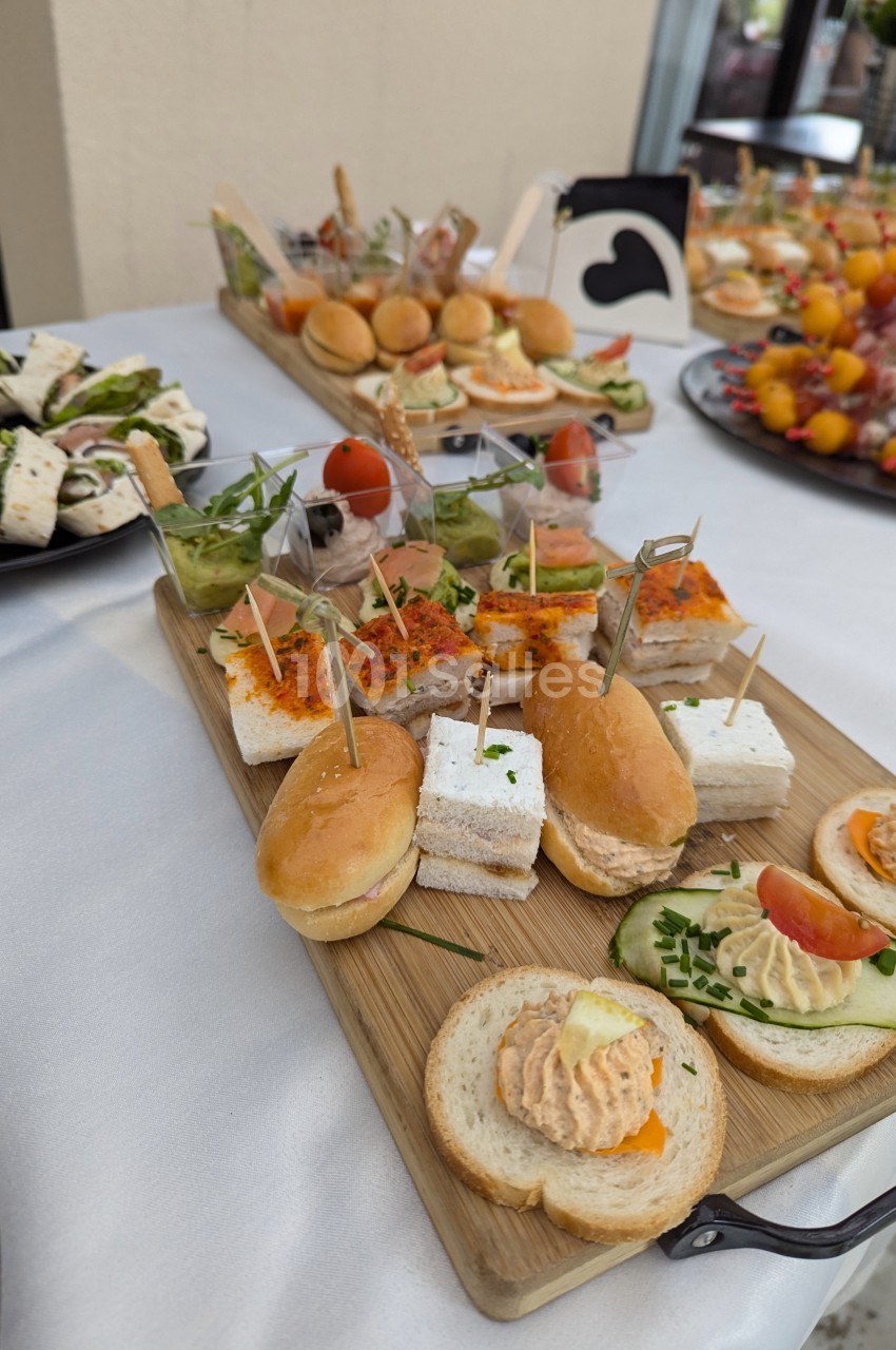 Plateau de canapés variés avec mini-sandwichs, toasts garnis et brochettes, disposé sur une table blanche.