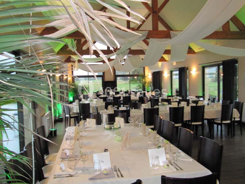 Salle de réception décorée avec des tables dressées, des chaises noires et des voilages suspendus au plafond.