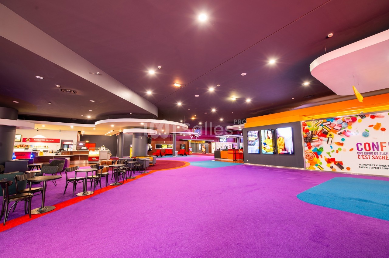 Espace intérieur lumineux avec moquette violette, tables, chaises et comptoirs de restauration au fond.