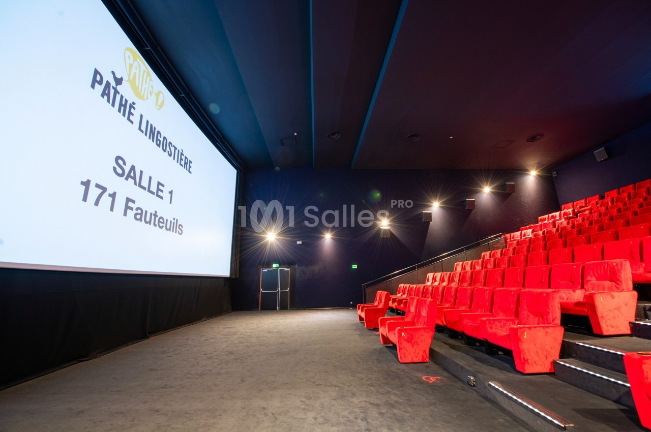 Salle de cinéma avec écran blanc, rangées de fauteuils rouges et éclairage tamisé.