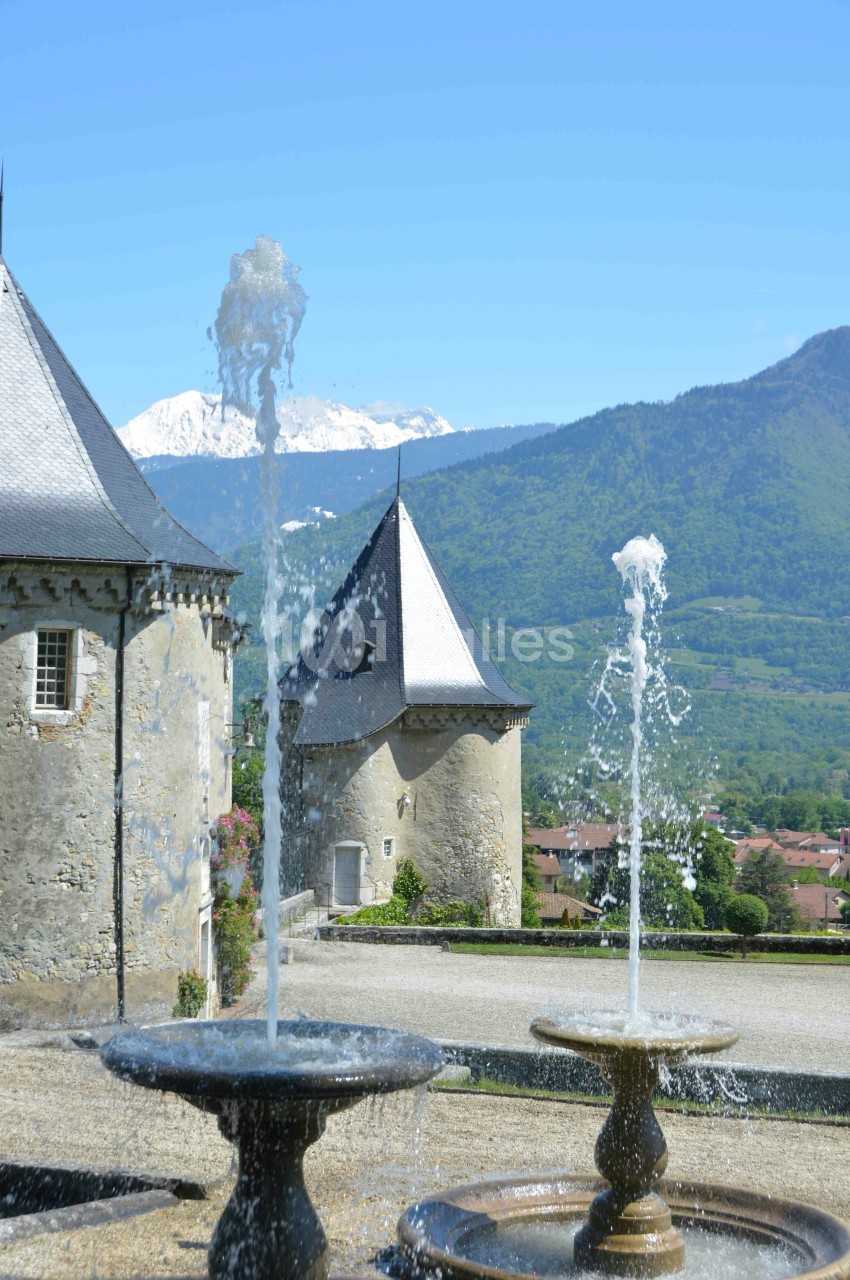 Fontaines jaillissantes devant des bâtiments historiques avec des montagnes enneigées en arrière-plan.