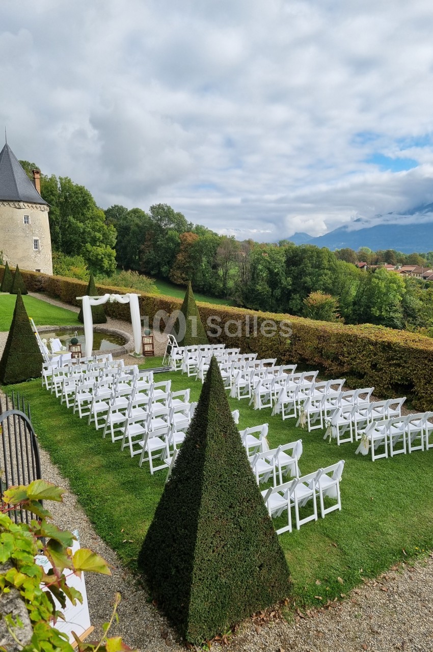 Chaises blanches alignées en extérieur pour une cérémonie, avec une arche décorée et un château en arrière-plan.