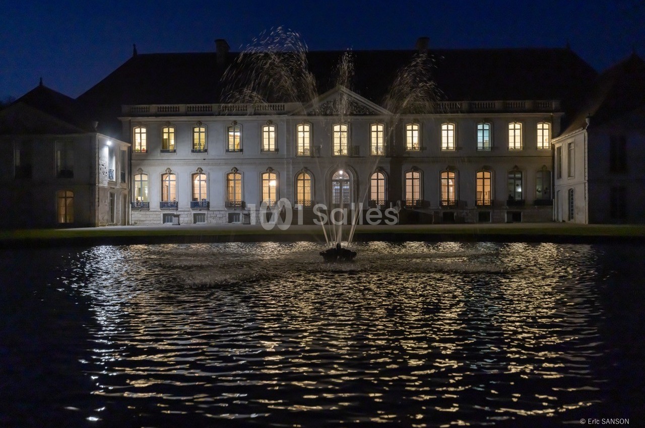 Façade éclairée d'un bâtiment historique avec une fontaine illuminée au premier plan, de nuit.