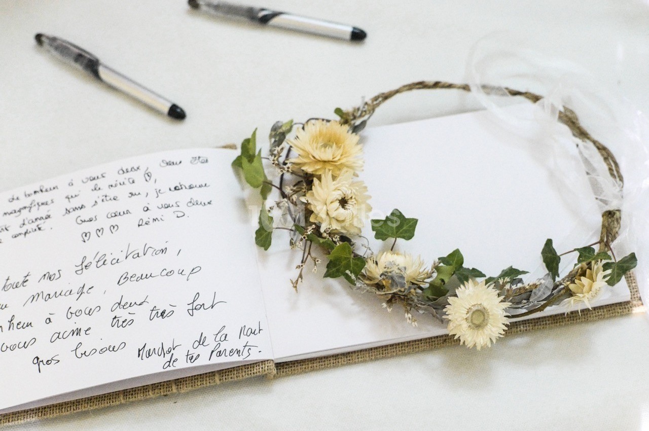 Couronne de fleurs séchées posée sur un carnet ouvert avec un message manuscrit et deux stylos en arrière-plan.