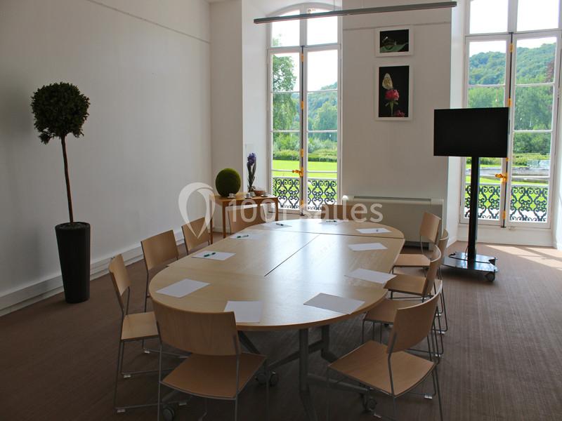 Salle de réunion lumineuse avec une table ovale, des chaises en bois, des fenêtres donnant sur un jardin verdoyant.