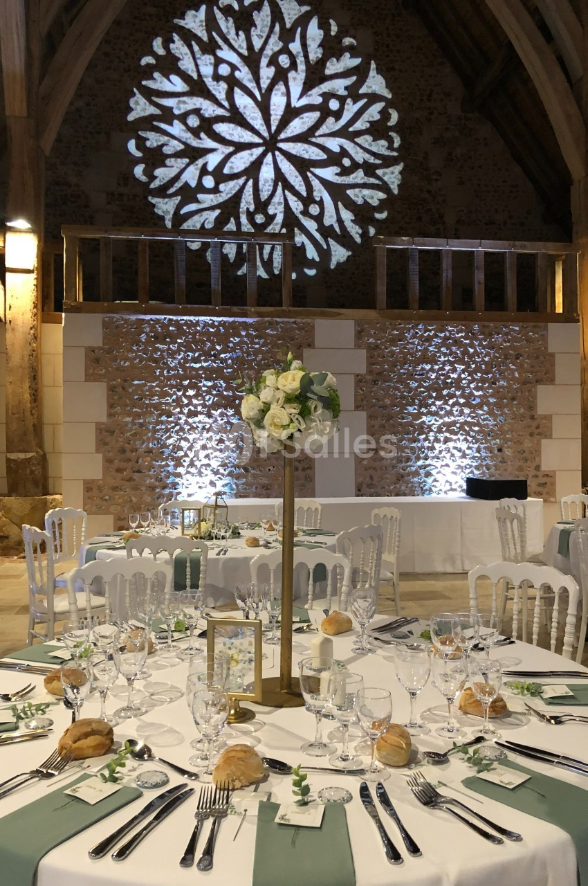 Salle de réception décorée avec des tables élégantes, nappes blanches, centres de table fleuris et éclairage chaleureux.