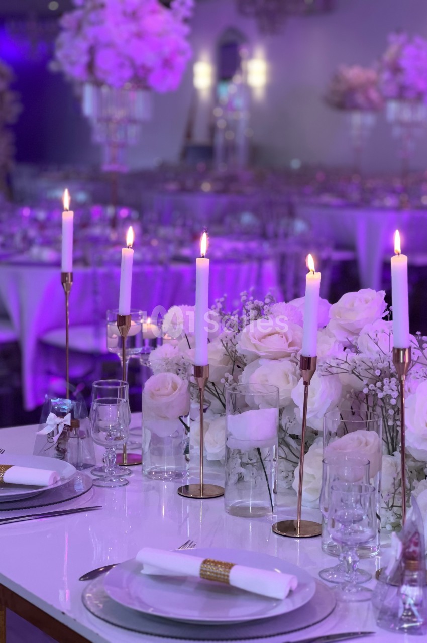 Table élégamment dressée avec chandeliers, roses blanches et vaisselle raffinée dans une salle décorée pour un événement.
