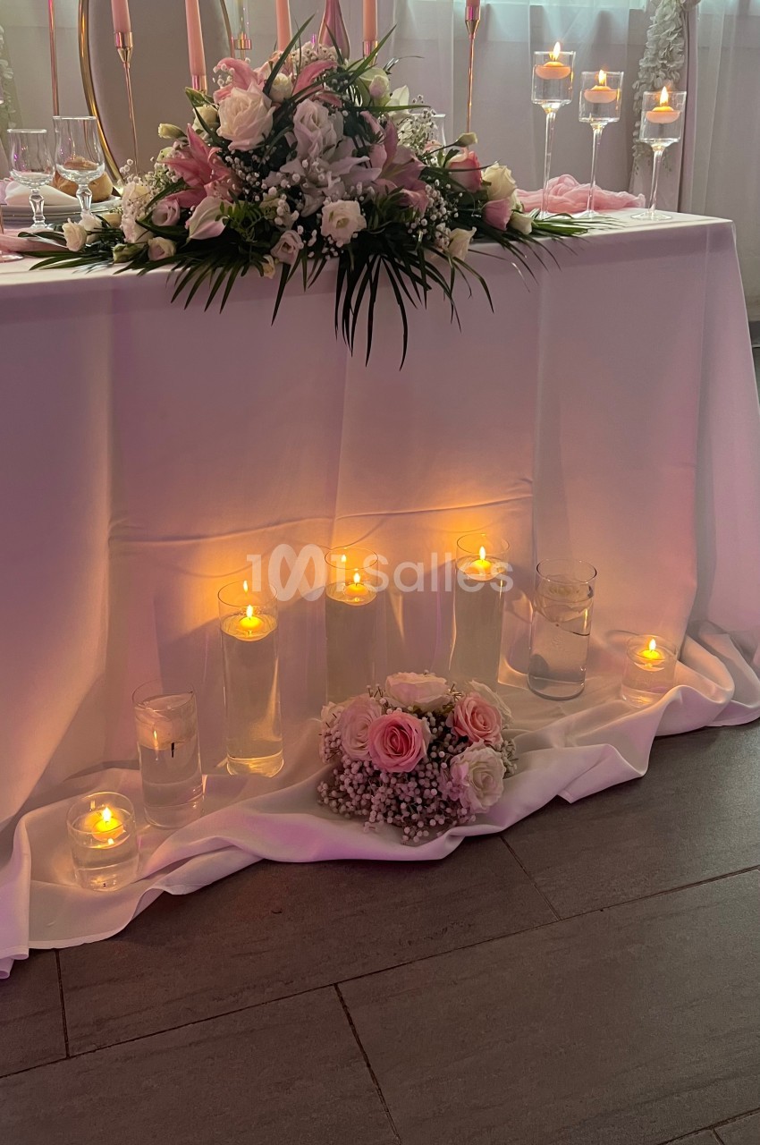 Table décorée pour un événement avec fleurs roses et blanches, bougies allumées et voilage en arrière-plan.