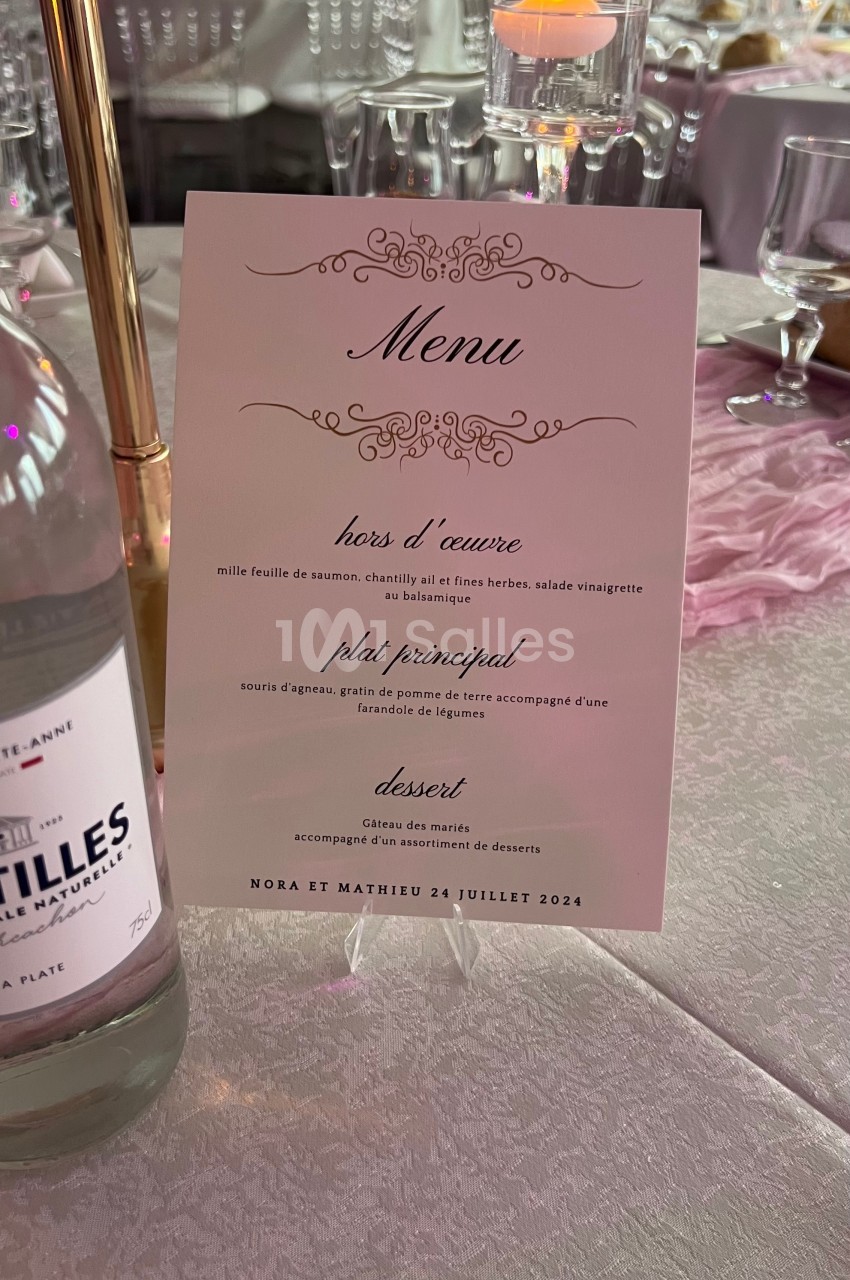 Carte de menu de mariage posée sur une table décorée avec des bougies, nappes blanches et éléments roses.