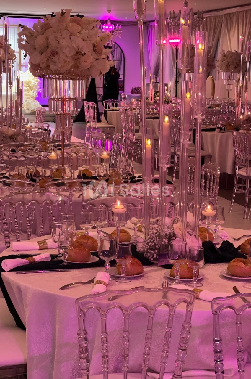 Salle de réception élégamment décorée avec tables dressées, chandeliers, fleurs blanches et éclairage tamisé.