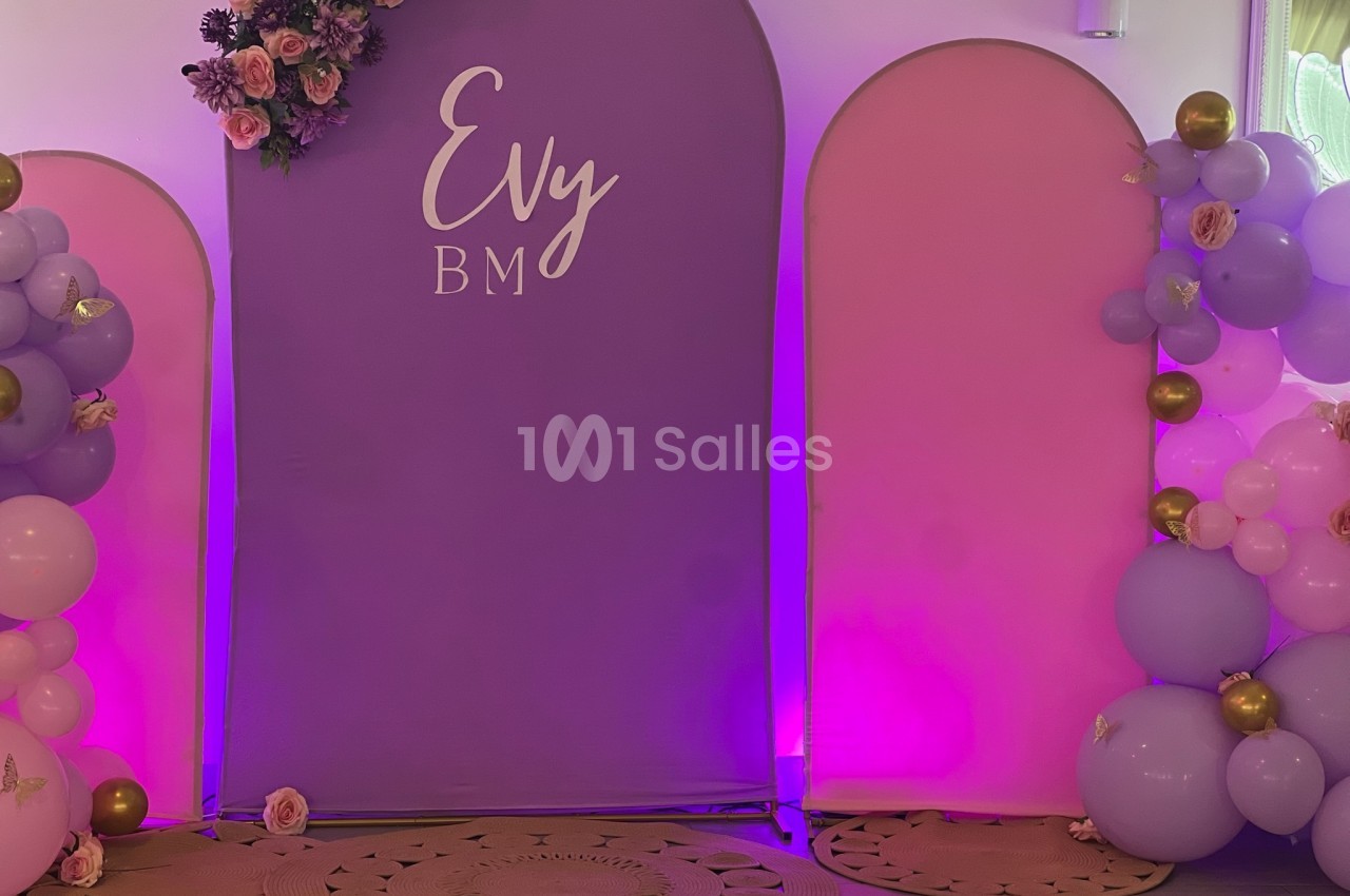 Mur décoratif avec panneaux roses et violets, ballons assortis et fleurs, utilisé pour un événement festif.