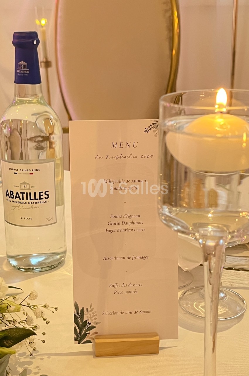 Bouteille d'eau, menu imprimé et bougie sur une table élégamment dressée pour un repas.