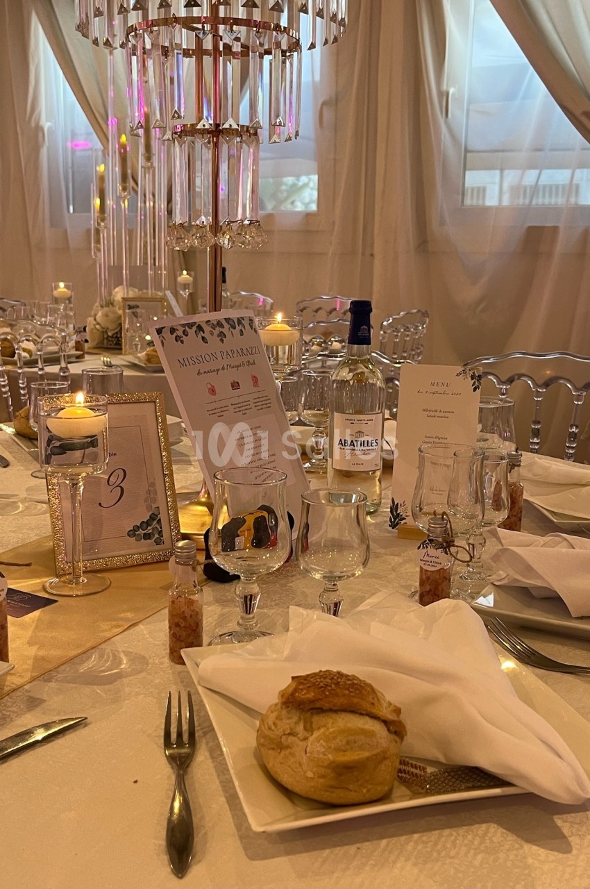 Table élégamment dressée pour un événement, avec décorations, chandeliers, menus et pain sur une assiette blanche.