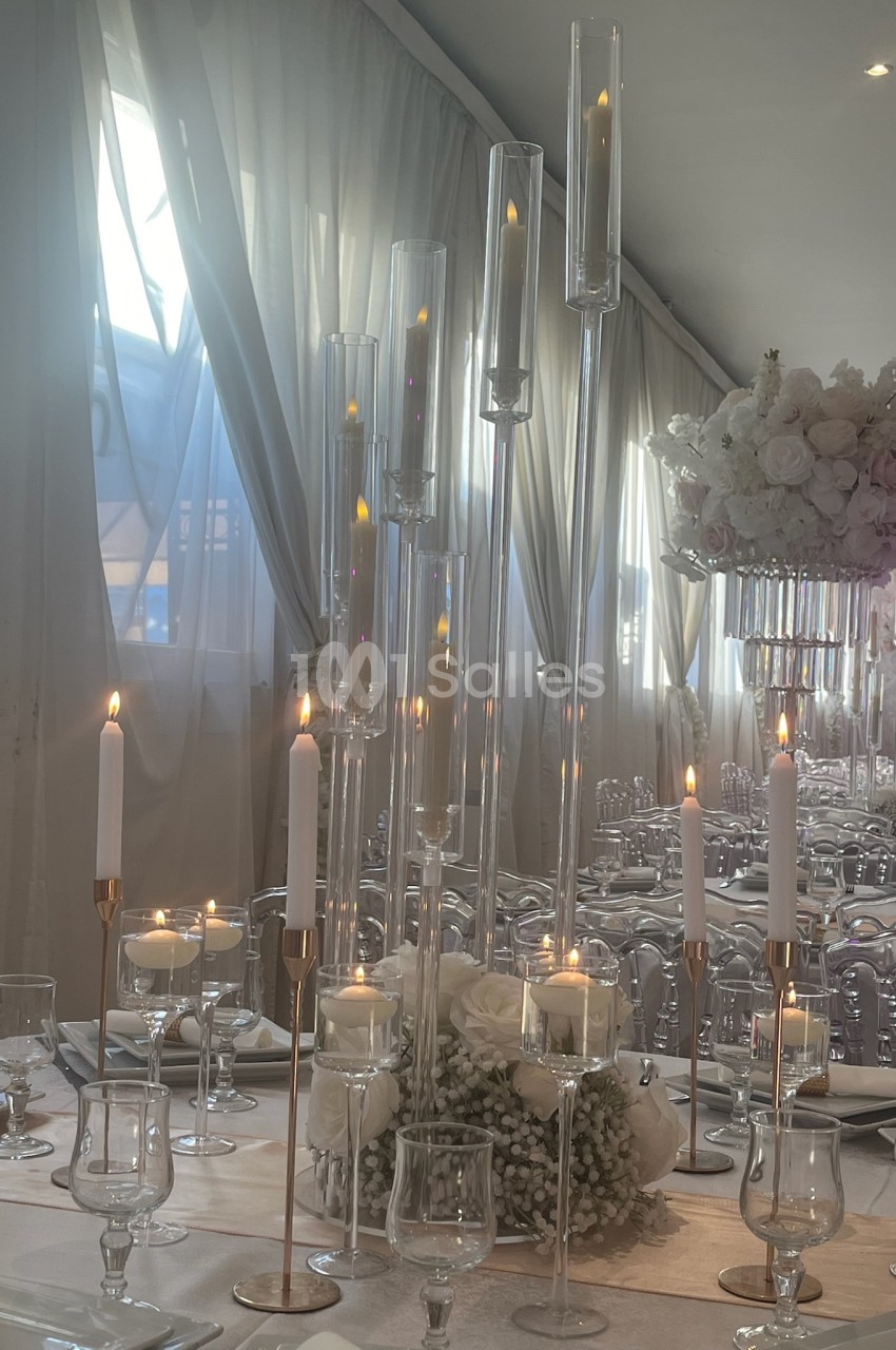 Bougies allumées et décorations florales blanches sur une table élégamment dressée dans une salle lumineuse.