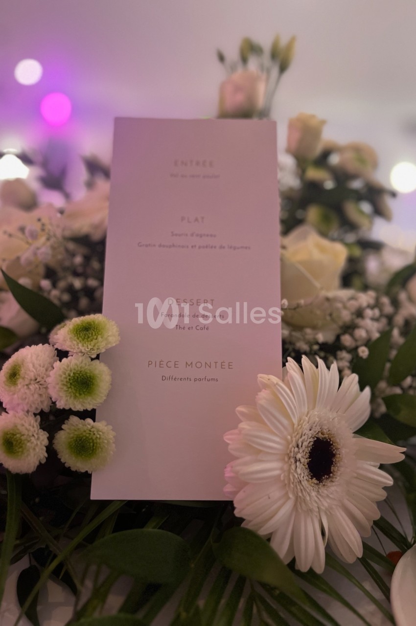 Menu imprimé sur une carte blanche entourée de fleurs blanches et vertes dans un décor lumineux.
