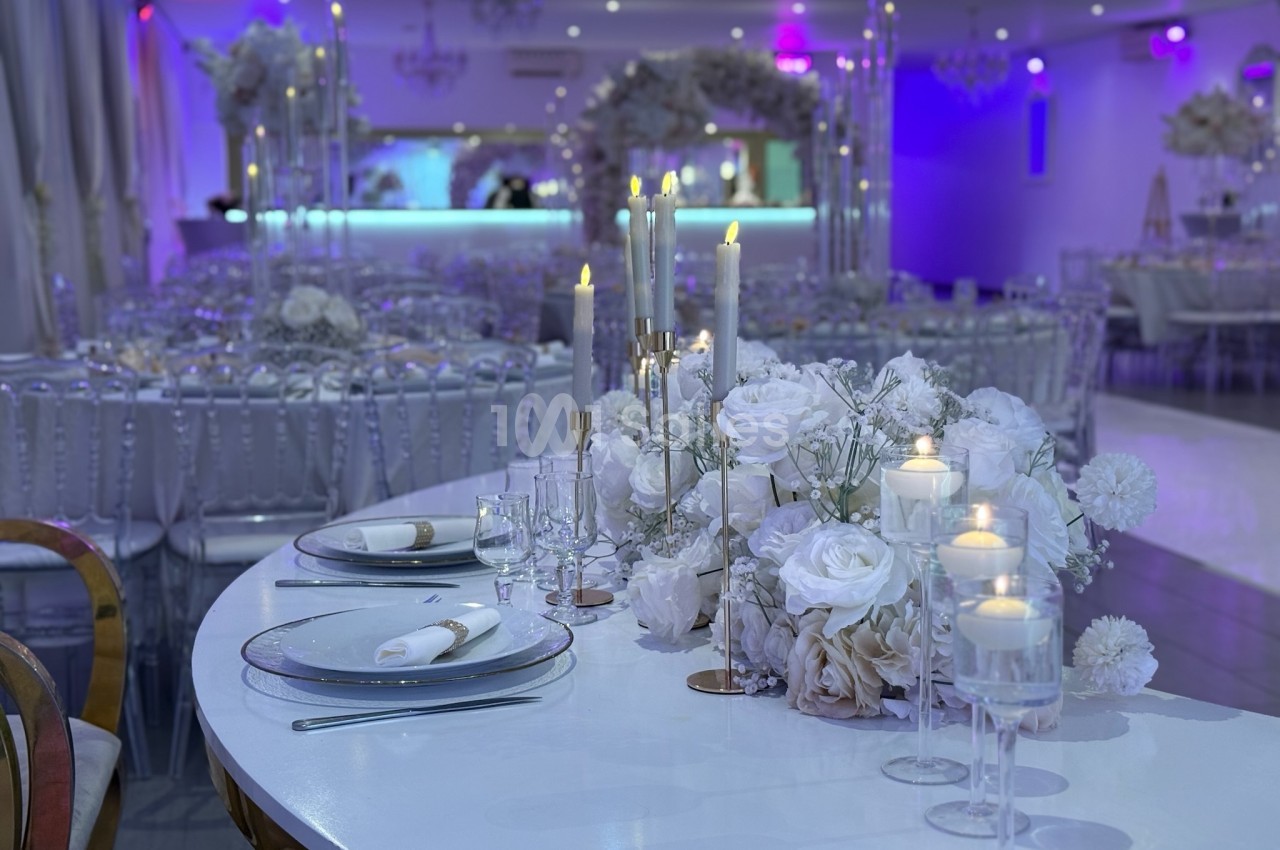 Salle de réception décorée avec des fleurs blanches, des chandeliers et des tables élégamment dressées.