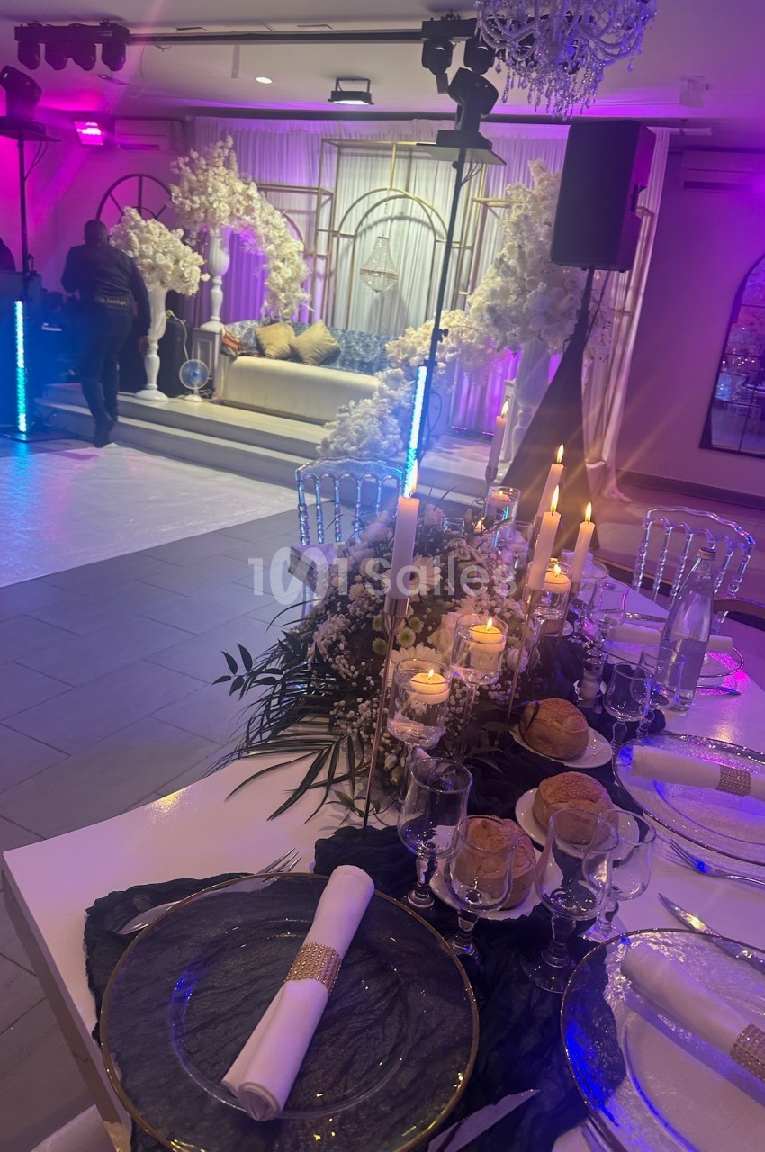 Table élégamment dressée avec bougies et décor floral, en arrière-plan un espace lounge décoré pour un événement festif.