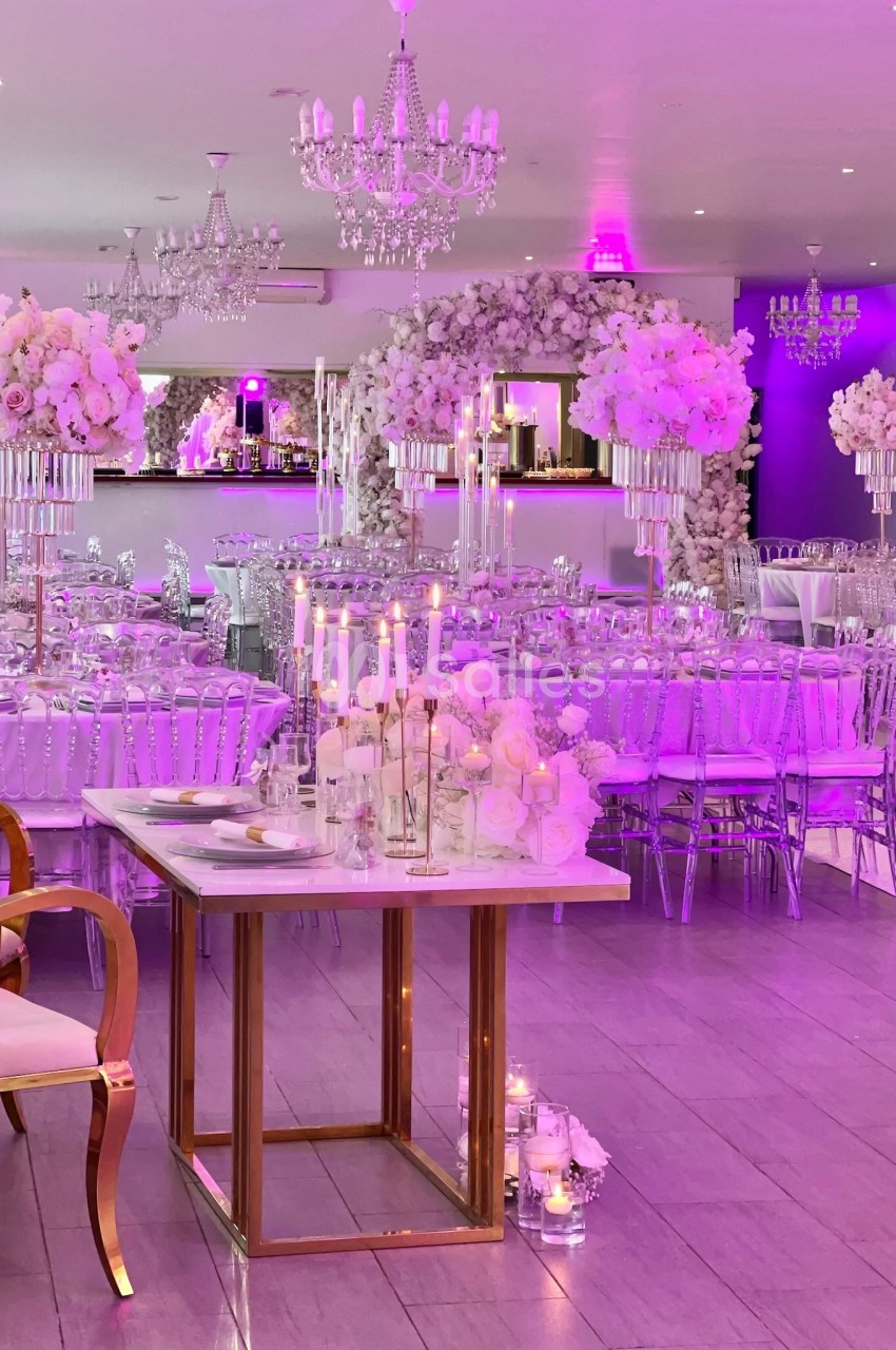 Salle de réception décorée avec des tons roses, chandeliers, fleurs blanches et tables élégamment dressées.
