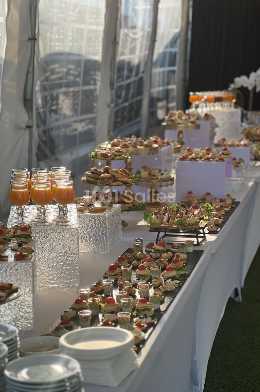 Buffet élégant avec verrines, amuse-bouches variés et boissons disposés sur une longue table blanche en extérieur.