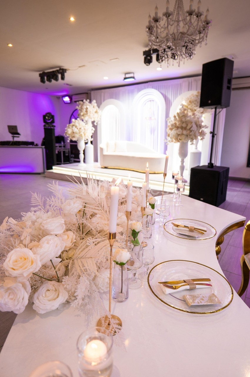 Table décorée avec des bougies, fleurs blanches et vaisselle élégante, dans une salle de réception lumineuse.