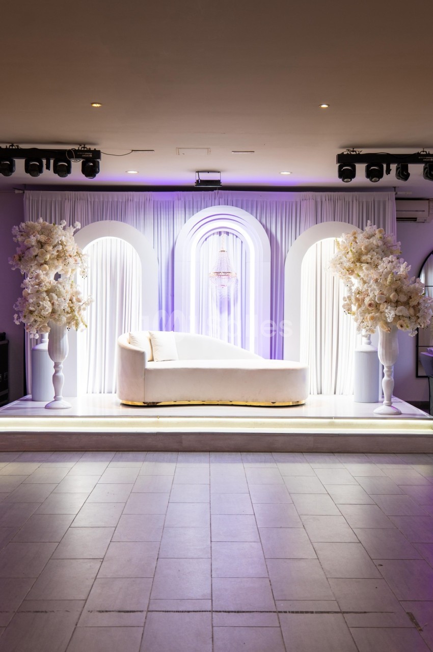 Canapé blanc sur une scène décorée de rideaux, arches lumineuses et arrangements floraux blancs.