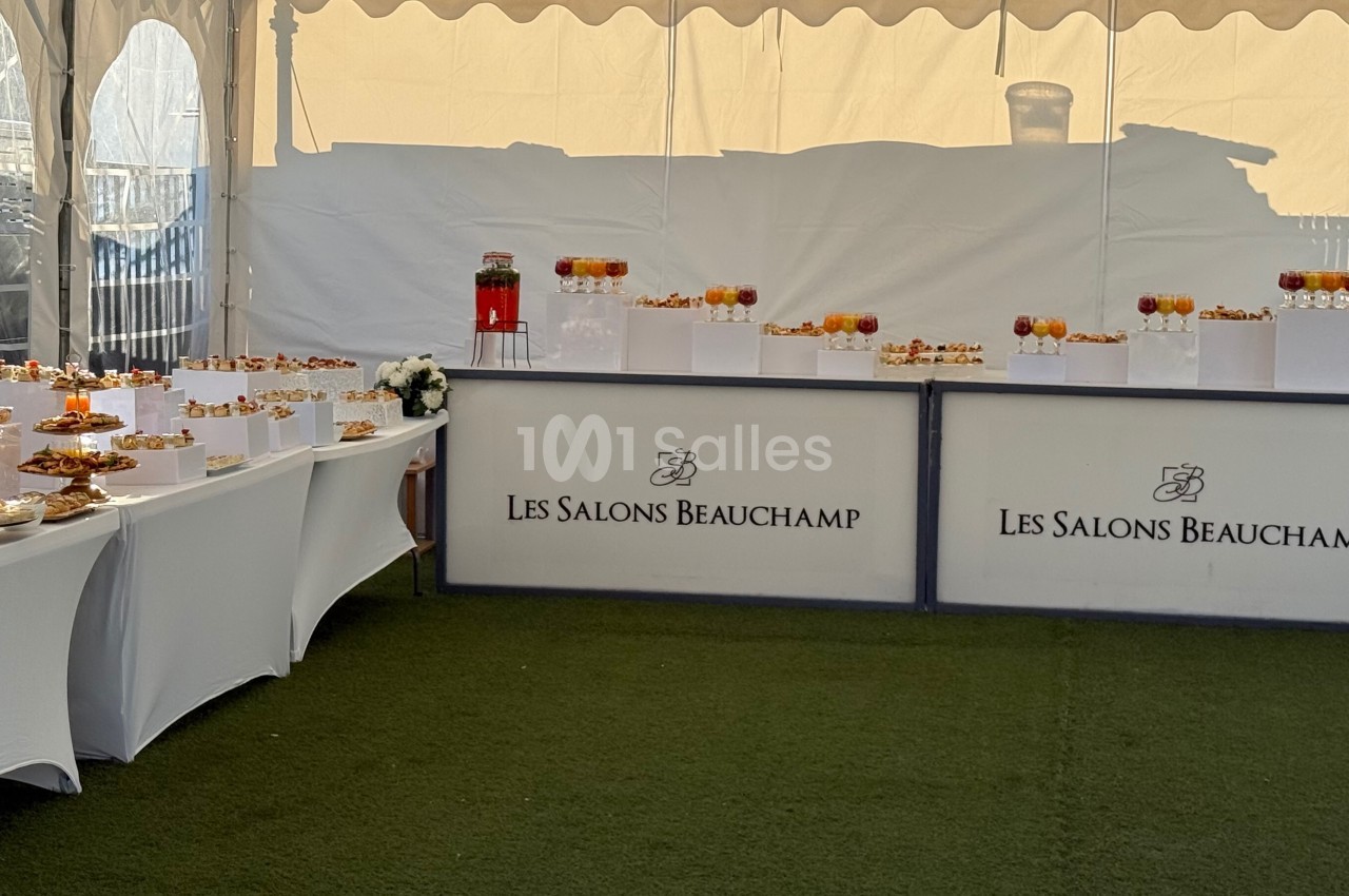 Buffet dressé sous une tente avec des boissons et des amuse-bouches sur des tables blanches.