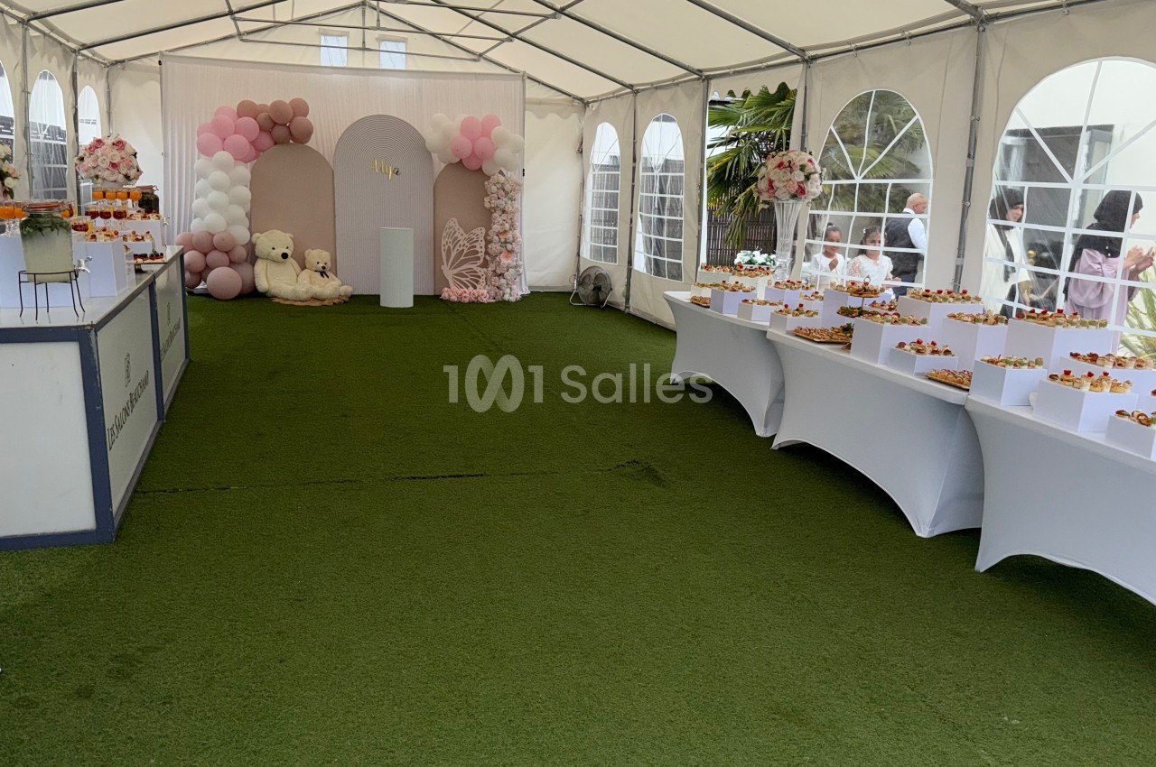 Intérieur d'une tente décorée pour un événement, avec tables de buffet, ballons et arrangements floraux.
