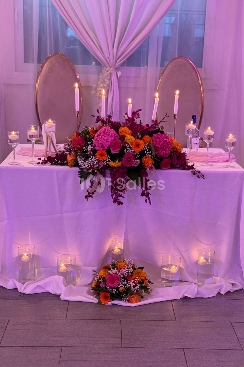 Table décorée pour un événement, ornée de fleurs colorées, bougies allumées et drapée de tissu blanc.