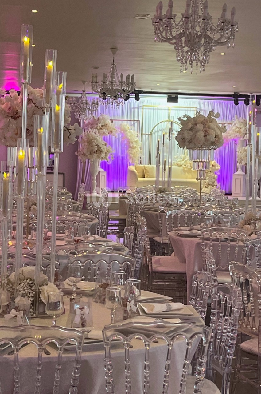 Salle de réception décorée avec des chandeliers, des fleurs blanches et des tables dressées pour un événement.