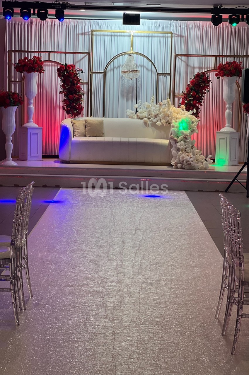 Canapé blanc décoré de fleurs blanches et rouges, placé sur une scène avec rideaux et éclairages colorés.