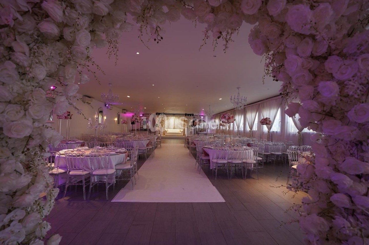 Salle de réception décorée pour un mariage, avec des tables élégantes, des fleurs blanches et une arche florale au premier…