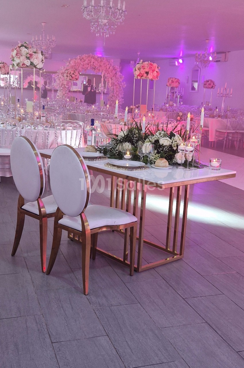 Table décorée avec des bougies et des fleurs, entourée de chaises blanches, dans une salle de réception élégante.