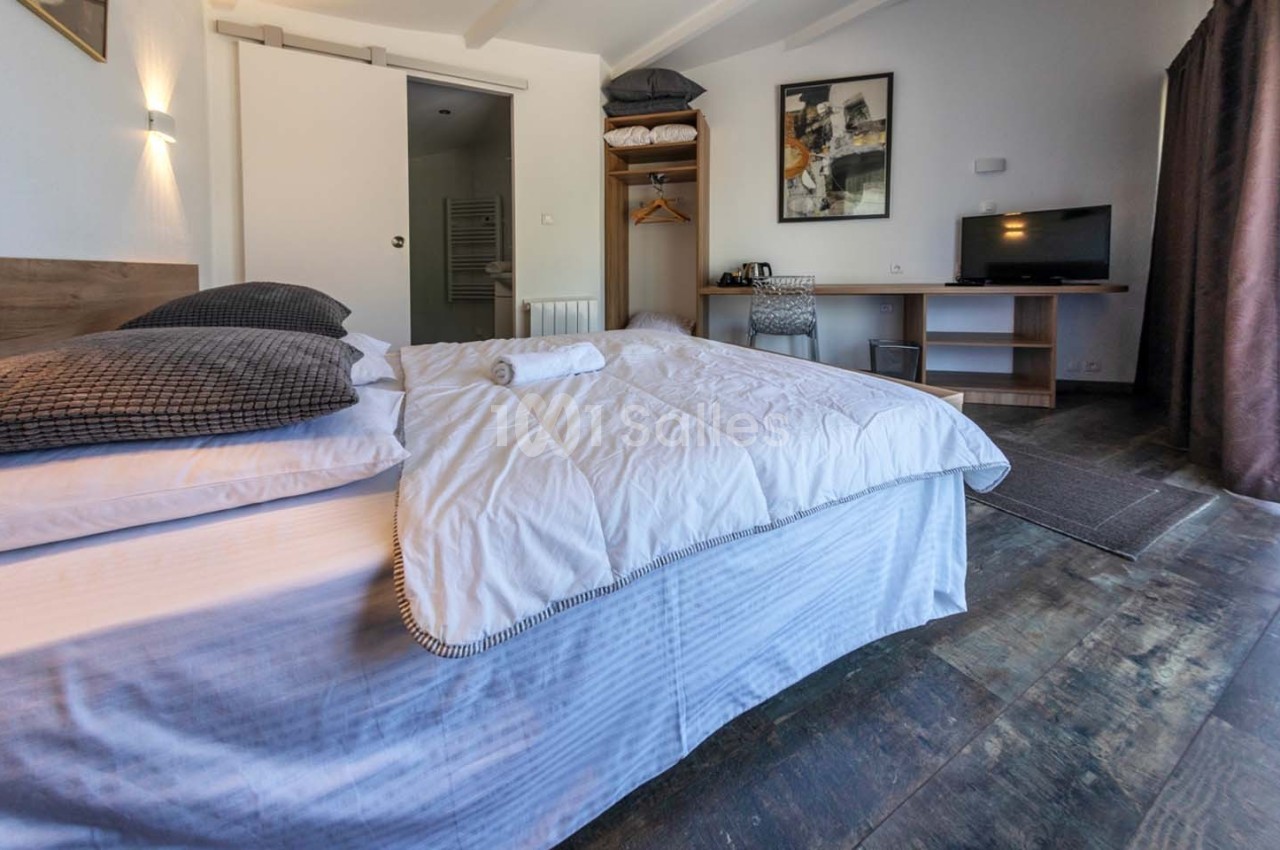 Chambre lumineuse avec lit double, bureau, télévision, armoire ouverte et porte donnant sur une salle de bain.