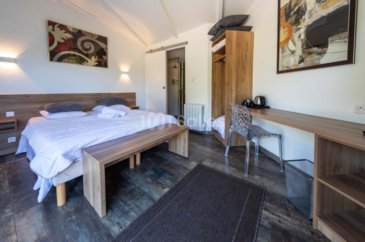 Chambre lumineuse avec lit double, bureau en bois, chaise, armoire ouverte et décoration murale abstraite.