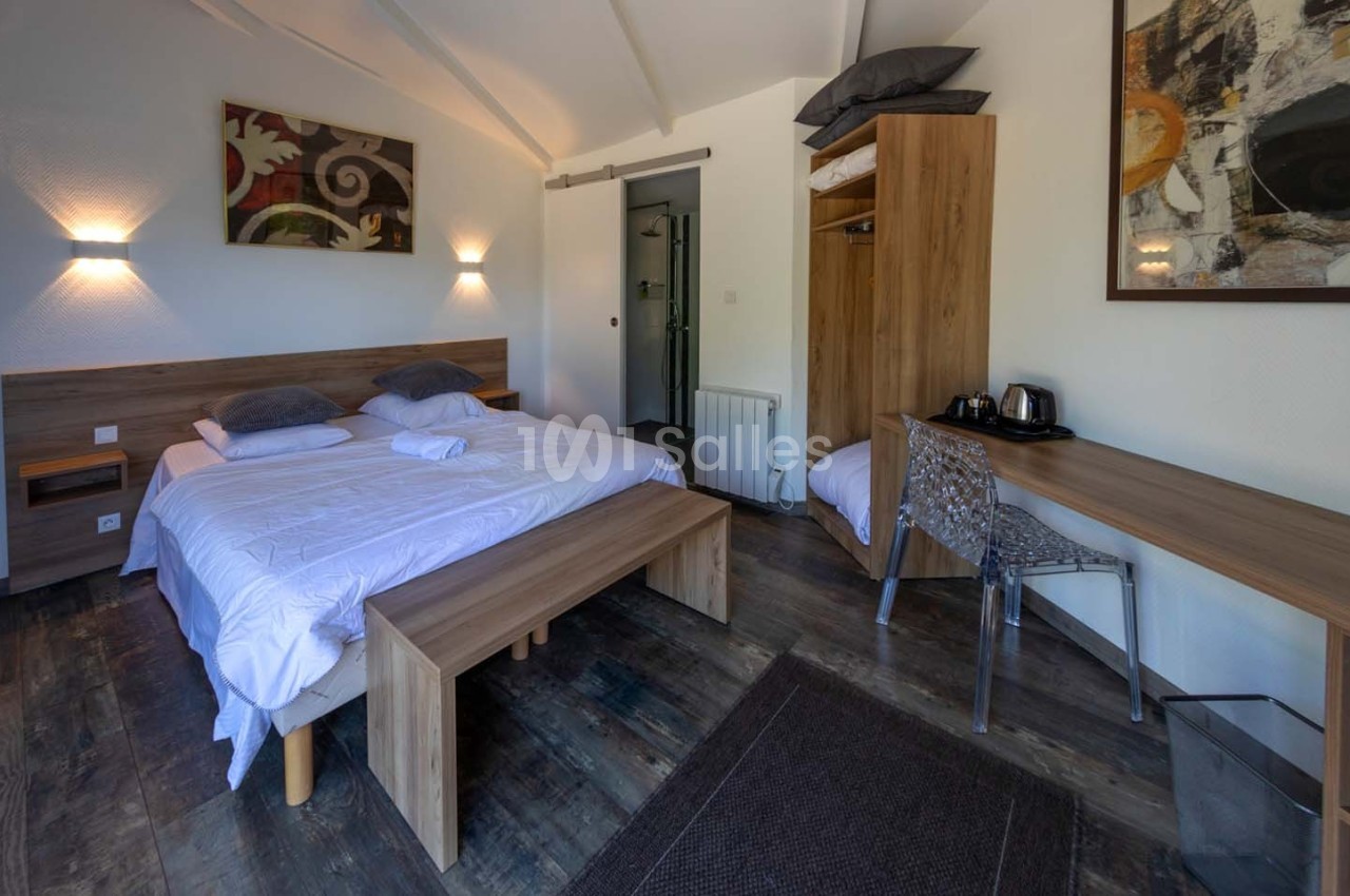 Chambre lumineuse avec lit double, bureau, chaise transparente, armoire ouverte et décoration murale abstraite.