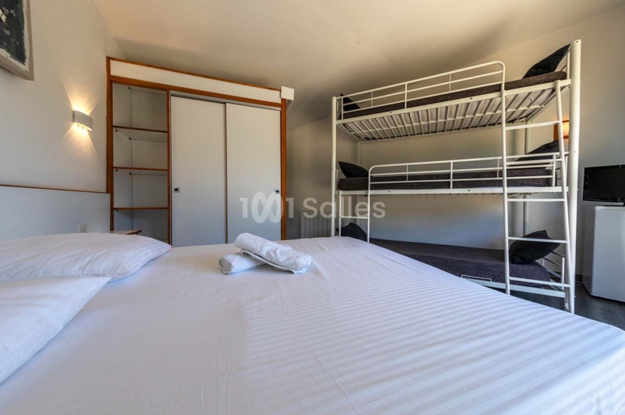 Chambre avec un lit double, des lits superposés, une armoire, un mini-réfrigérateur et des serviettes pliées sur le lit.
