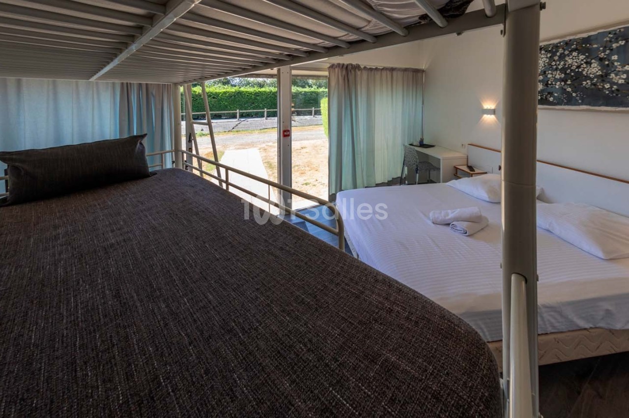 Lit superposé et lit double dans une chambre lumineuse avec vue sur l'extérieur, rideaux ouverts et décoration murale.