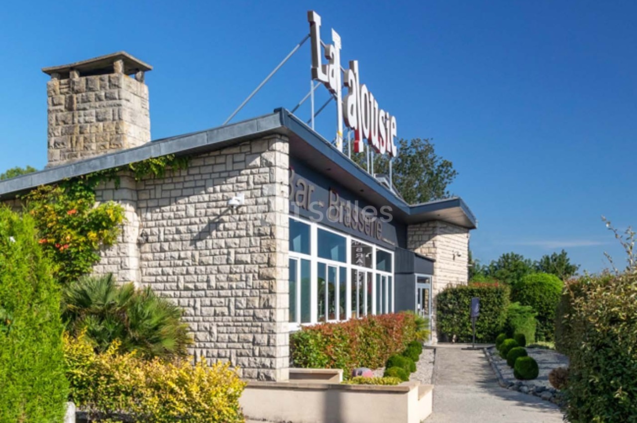 Façade d'un restaurant en pierre avec enseigne ’La Dousse’, entouré de verdure sous un ciel bleu.