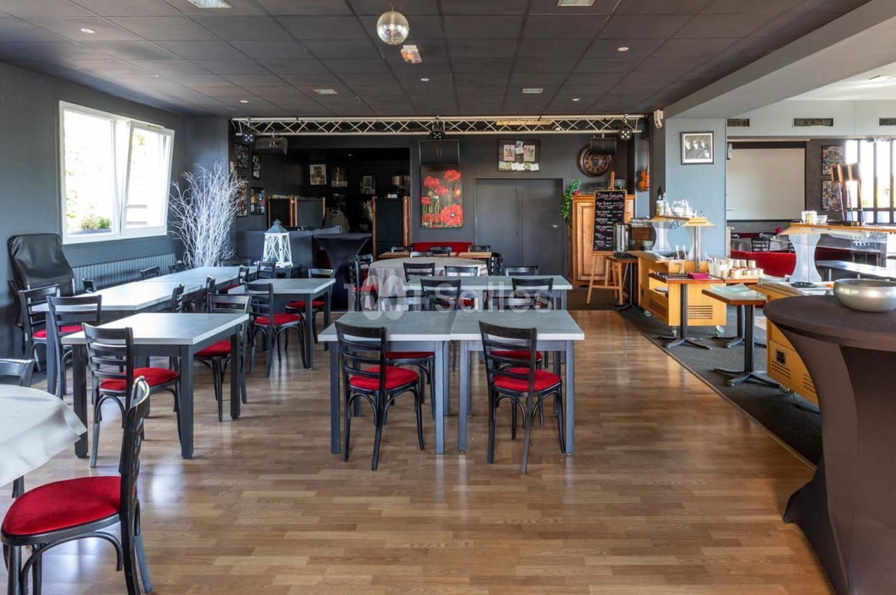 Salle de restaurant lumineuse avec tables et chaises noires, parquet en bois clair et buffet en arrière-plan.