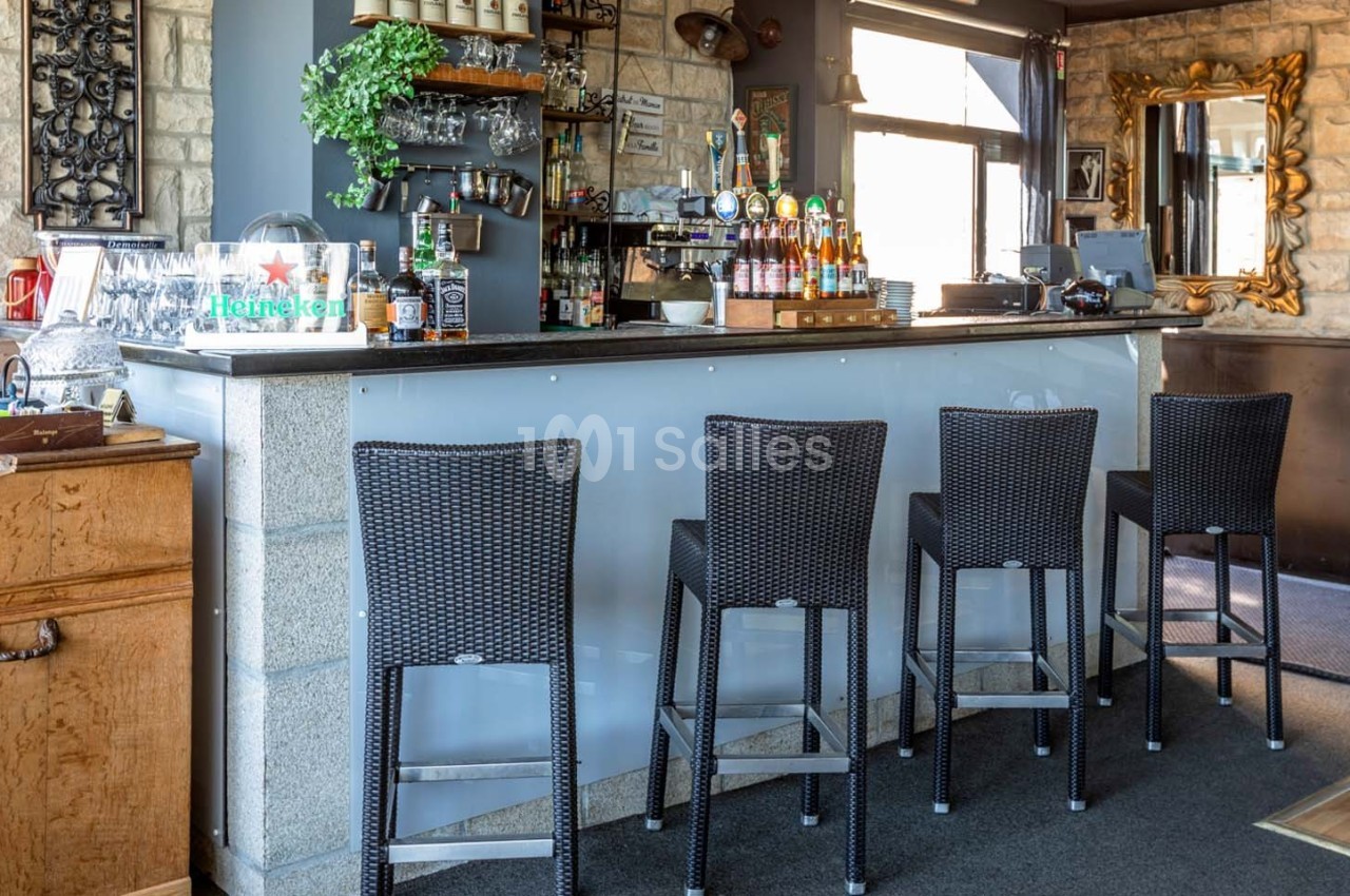 Comptoir de bar moderne avec tabourets en osier, étagères garnies de bouteilles et décoration murale en pierre.