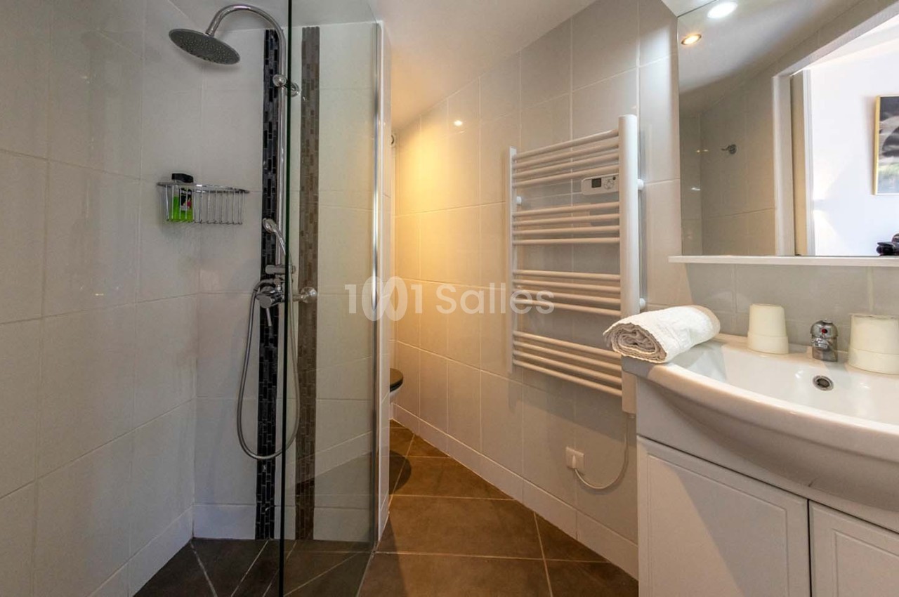 Salle de bain moderne avec douche à l'italienne, lavabo avec miroir, radiateur sèche-serviettes et carrelage clair.