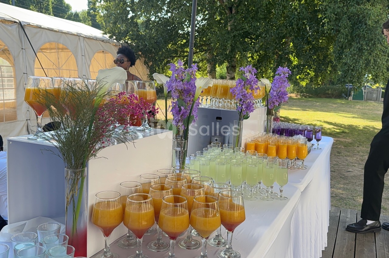 Table dressée en extérieur avec des verres de cocktails colorés, décorée de fleurs et entourée de verdure.
