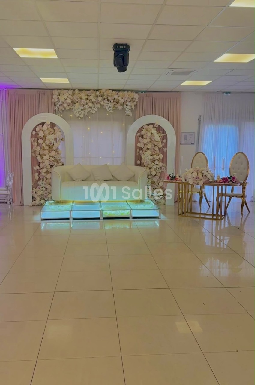 Salle de réception décorée avec un canapé blanc, des arches fleuries et une table élégante sur un sol carrelé.