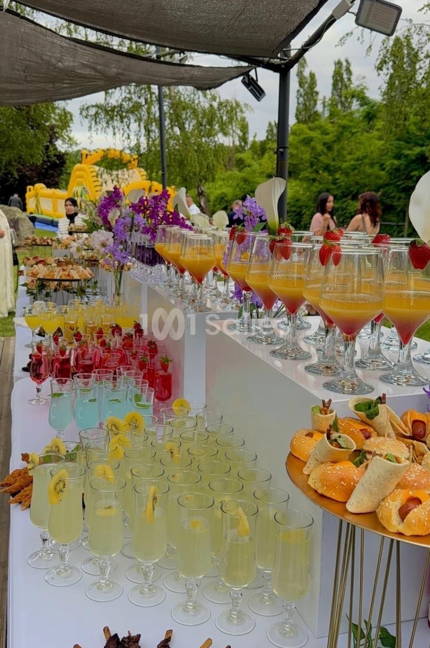 Buffet en extérieur avec cocktails colorés, brochettes, amuse-bouches et décorations florales sous une tonnelle.