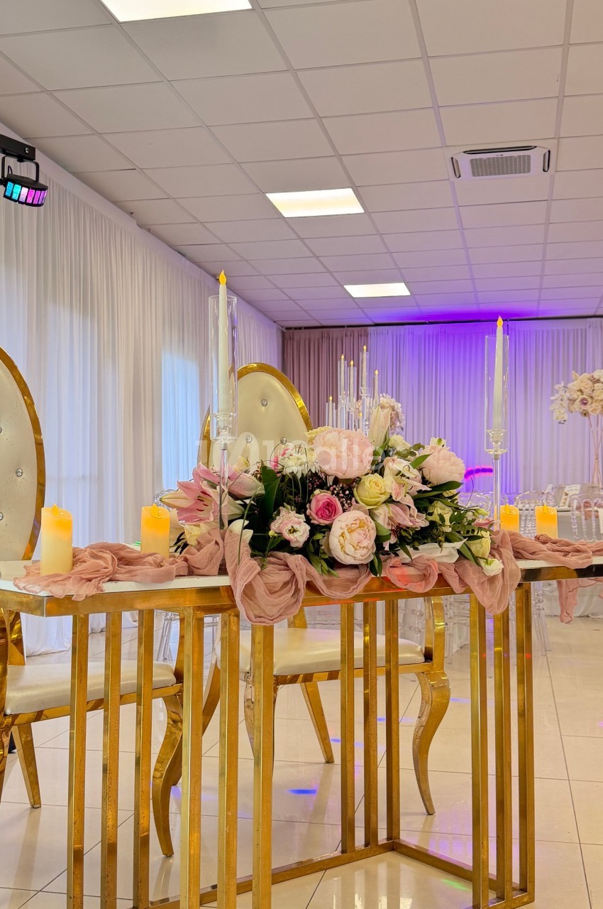 Table décorée avec des fleurs roses et blanches, bougies allumées et chaises élégantes dans une salle lumineuse.