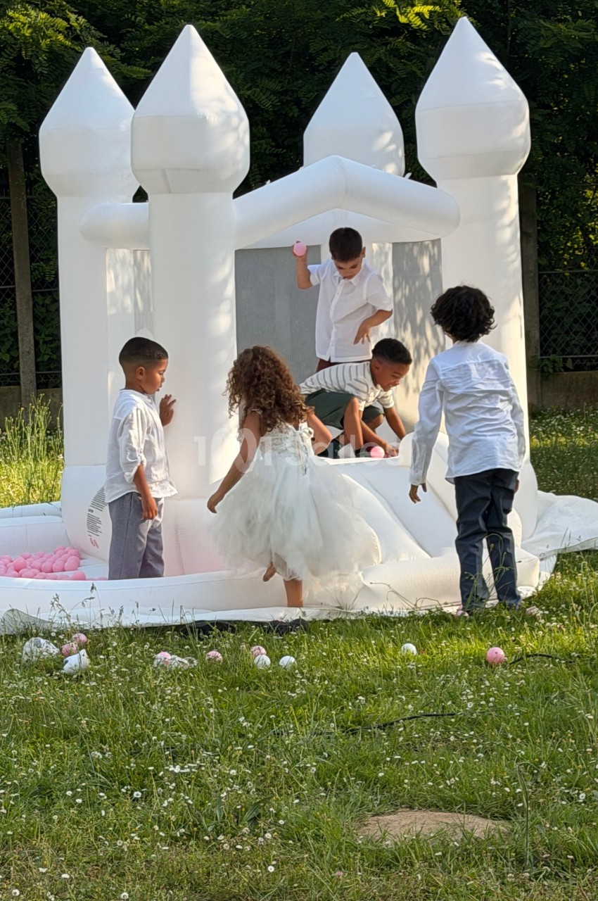 Des enfants jouent autour et à l'intérieur d'un château gonflable blanc dans un jardin verdoyant.