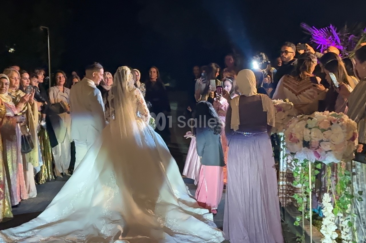 Un couple de mariés avance au milieu d'invités vêtus de tenues traditionnelles lors d'une célébration nocturne.