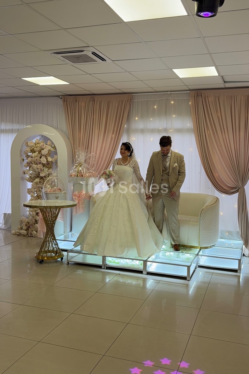 Un couple en tenue de mariage pose sur une estrade décorée avec des rideaux roses et des fleurs.