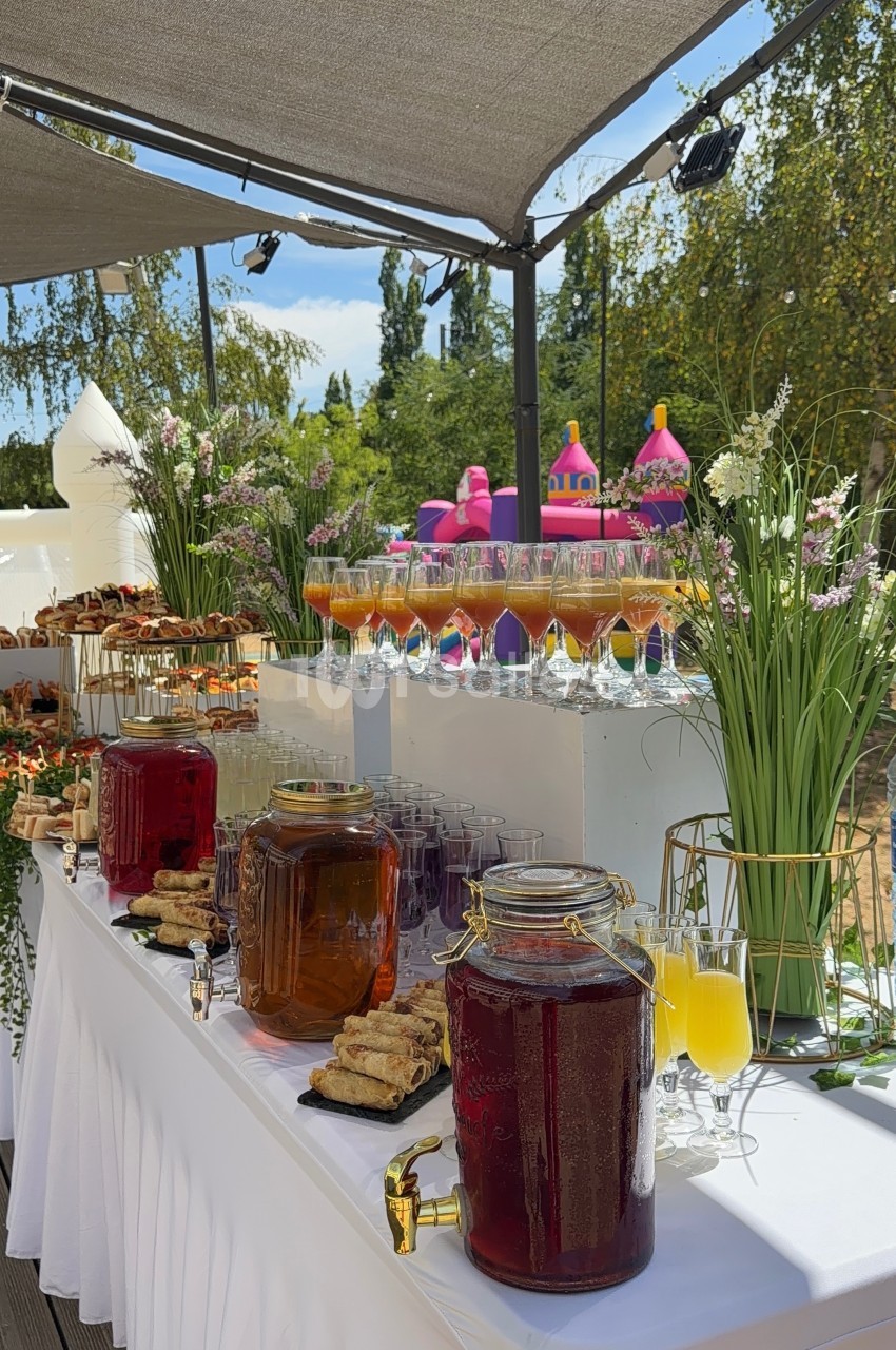 Buffet en extérieur avec boissons, verrines, pâtisseries et décorations florales sous une pergola.
